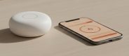 Hvid smart home-hub og smartphone med styringsapp p&aring; lyst tr&aelig;bord